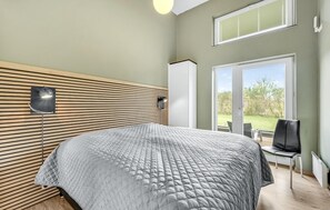 A modern bedroom with a large bed, a wall-mounted lamp, and a view of the outdoors through a sliding door. - Lovely home in Hemmet with sauna (Hemmet)