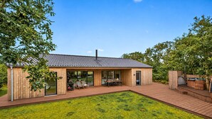 A modern wooden house with a tiled roof, a deck, and a grassy yard. - Beautiful home in Skjern with sauna (Skjern)
