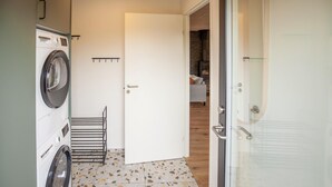 A laundry room with a washing machine, drying rack, and a door leading to a living area with a sofa. - Beautiful home in Skjern with sauna (Skjern)