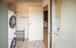 A laundry room with a washing machine, drying rack, and a door leading to a living area with a sofa. - Beautiful home in Skjern with sauna (Skjern)