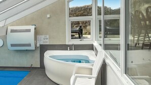 A modern bathroom with a built-in hot tub, a window with a view of the outdoors, and a white chair. - Pet friendly home in Hvide Sande with sauna (Hvide Sande)