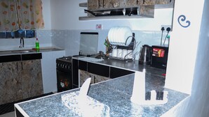 Una cocina con encimeras de granito, estufa, pileta y escurreplatos.