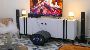 Una sala de estar moderna con un televisor de pantalla plana, dos lámparas de pie, un mueble blanco para entretenimiento y un subwoofer.
