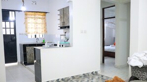Una cocina moderna con una isla central, un área de comedor con alfombra estampada y un dormitorio con cama y mesita de noche.