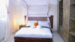Una cama bien hecha con dosel, una mesita de noche con lámpara, y un armario con fachada de piedra.