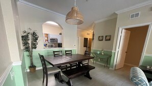 Ein Essbereich mit Holztisch und Stühlen, einer Hängeleuchte und Blick in eine Küche mit Mikrowelle und Schränken.