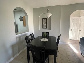 Een eetruimte met een tafel, stoelen, een hanglamp en een deur op de achtergrond.
