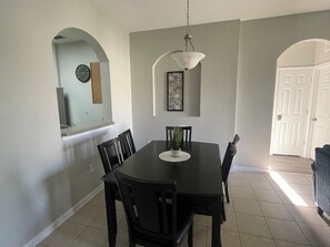 Un coin repas avec une table, des chaises, un luminaire suspendu et une porte en arrière-plan.