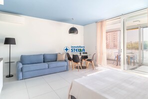 A modern living room with a sofa, a dining table with chairs, a lamp, and a logo for 'immobiliere STECK'.