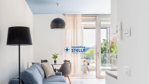 Moderni olohuone, jossa on sohva, lamppu, ruokapöytä tuoleineen ja lasiovesta avautuva näkymä ulos.