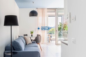 Una sala moderna con sofá, lámpara, mesa de comedor con sillas y vistas al exterior a través de un ventanal.