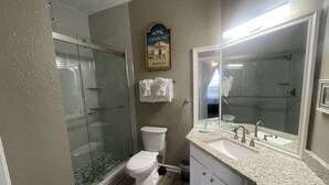 Ein Badezimmer mit Duschkabine, Toilette, Waschbecken mit großem Spiegel und Handtuchhalter.