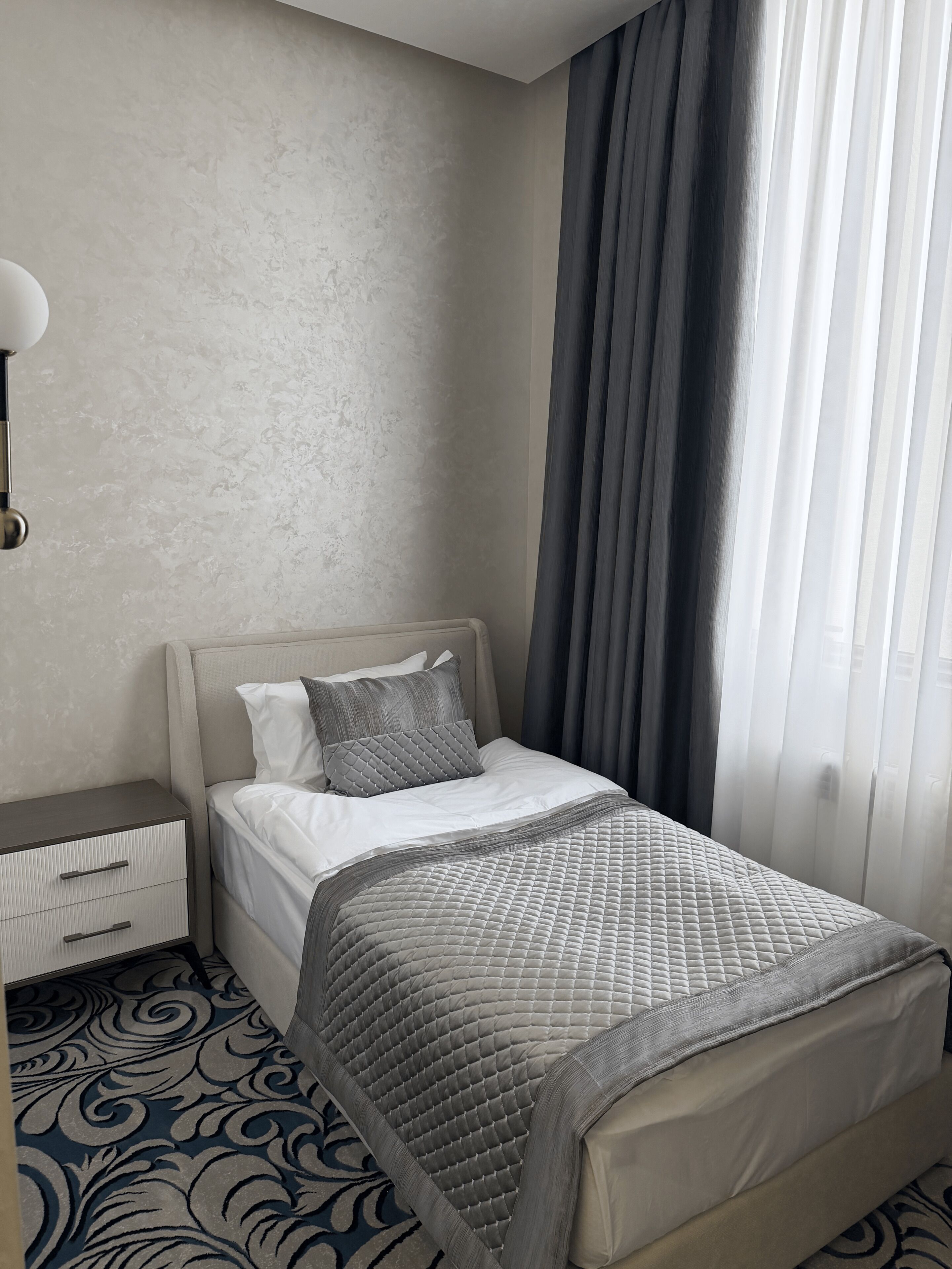 A hotel room with a bed, a nightstand, a lamp, and a patterned carpet.