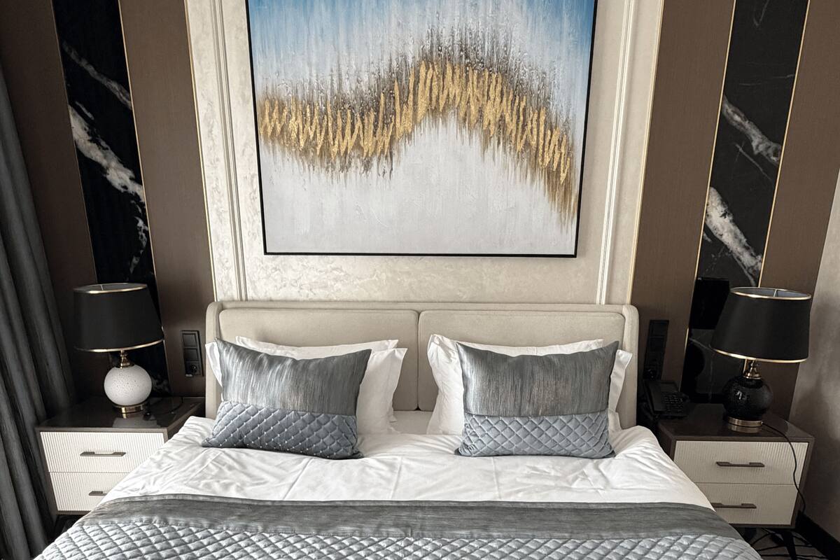 A hotel room with a large bed, two bedside tables, a painting on the wall, and marble paneling.