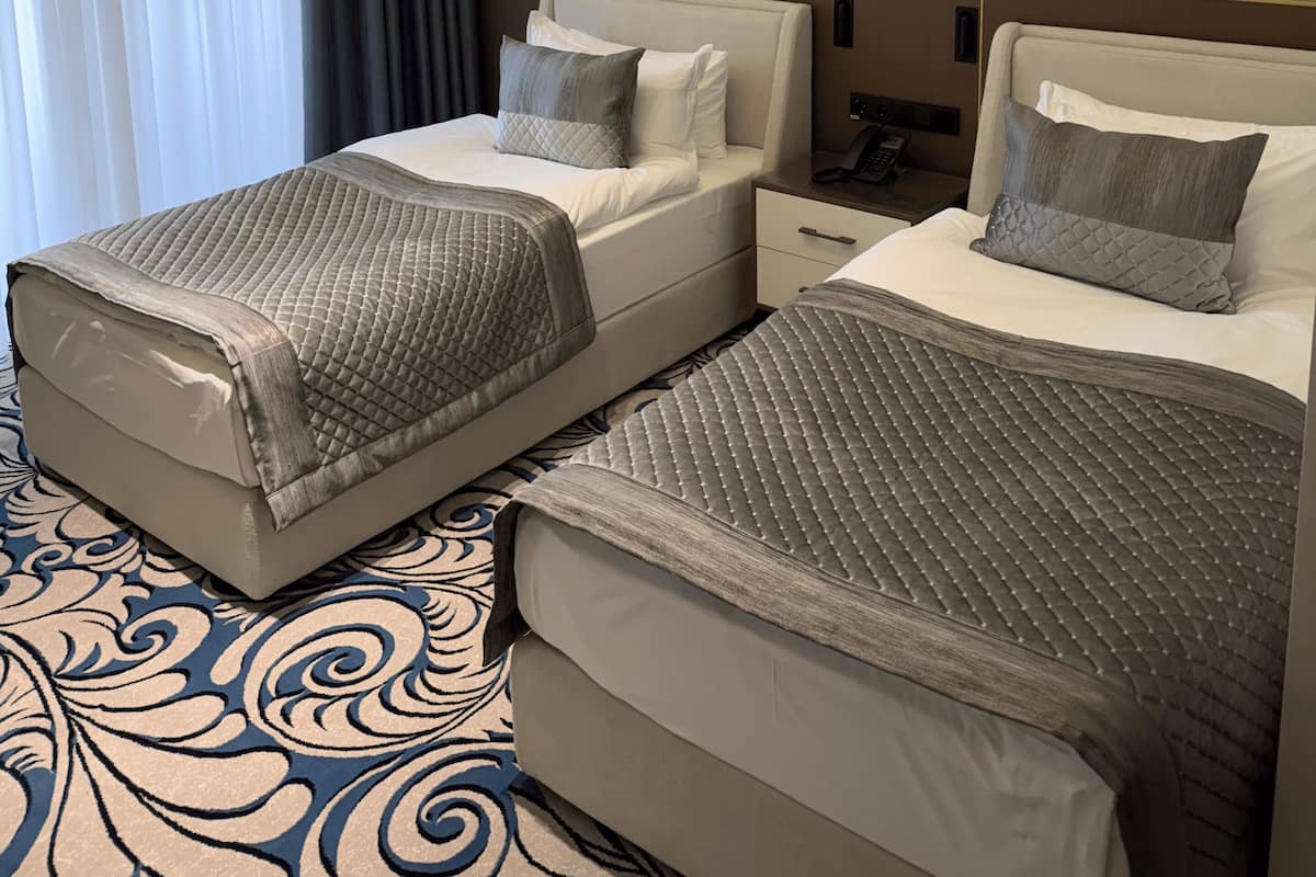 A hotel room with two beds, a large abstract painting, a patterned carpet, and a window with curtains.