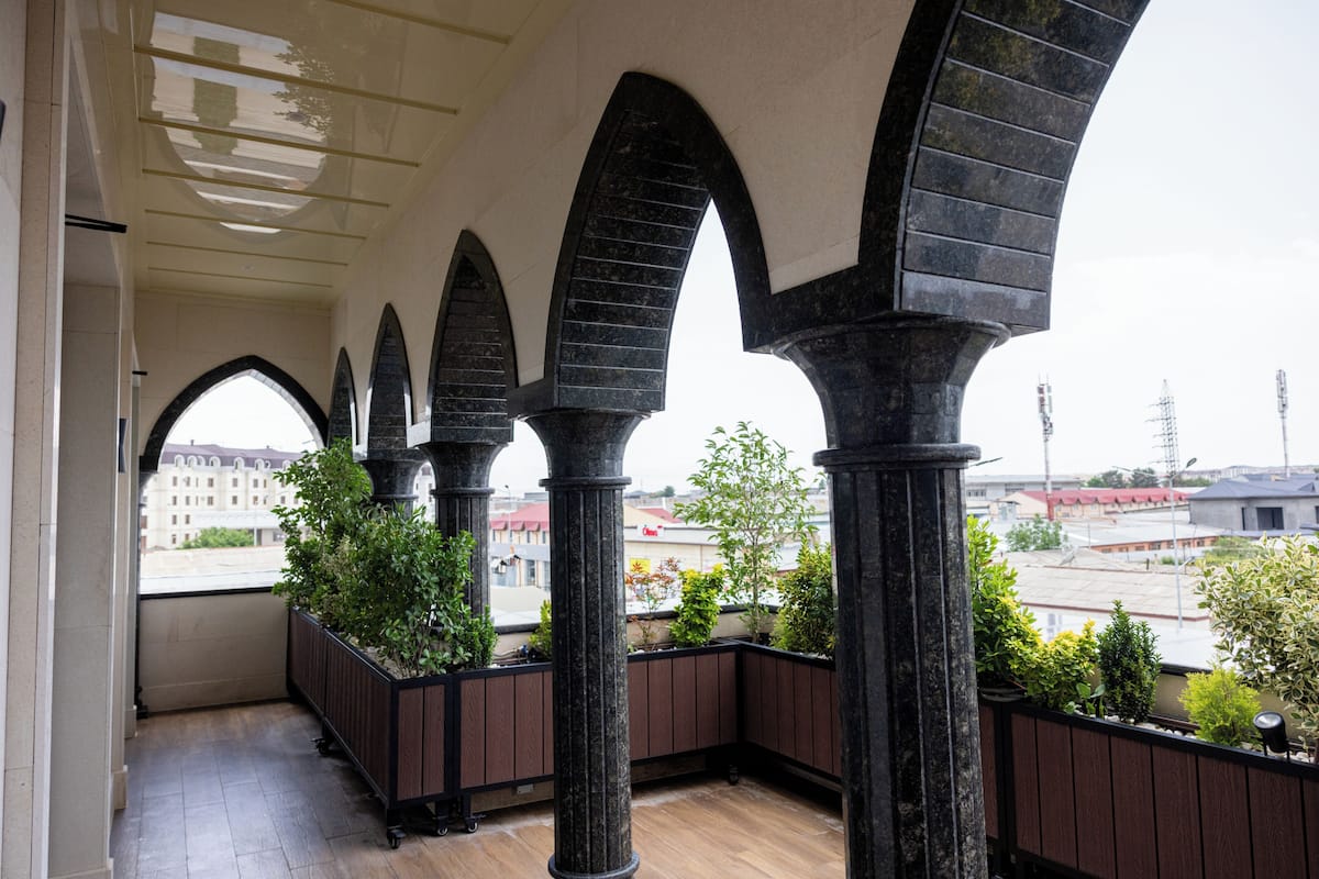 A balcony with a view of the city, featuring a series of arches and potted plants.