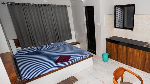 A bedroom with a bed, a ceiling fan, a bathroom door, and a kitchenette area.