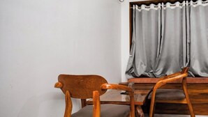 A corner room with a wooden dining table and chairs, a window with grey curtains, and a wall-mounted air conditioner.