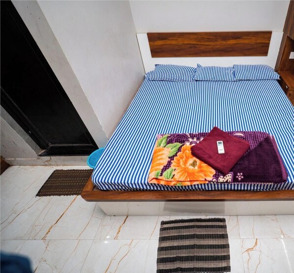 Una cama con cabecera de madera, colcha a rayas azul y blanca, y una manta doblada de colores sobre la cama.