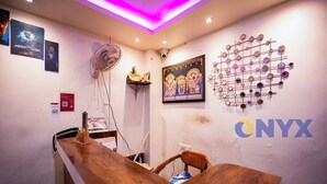 A reception area with a wooden reception desk, a wall-mounted fan, framed artwork, and a decorative wall piece.