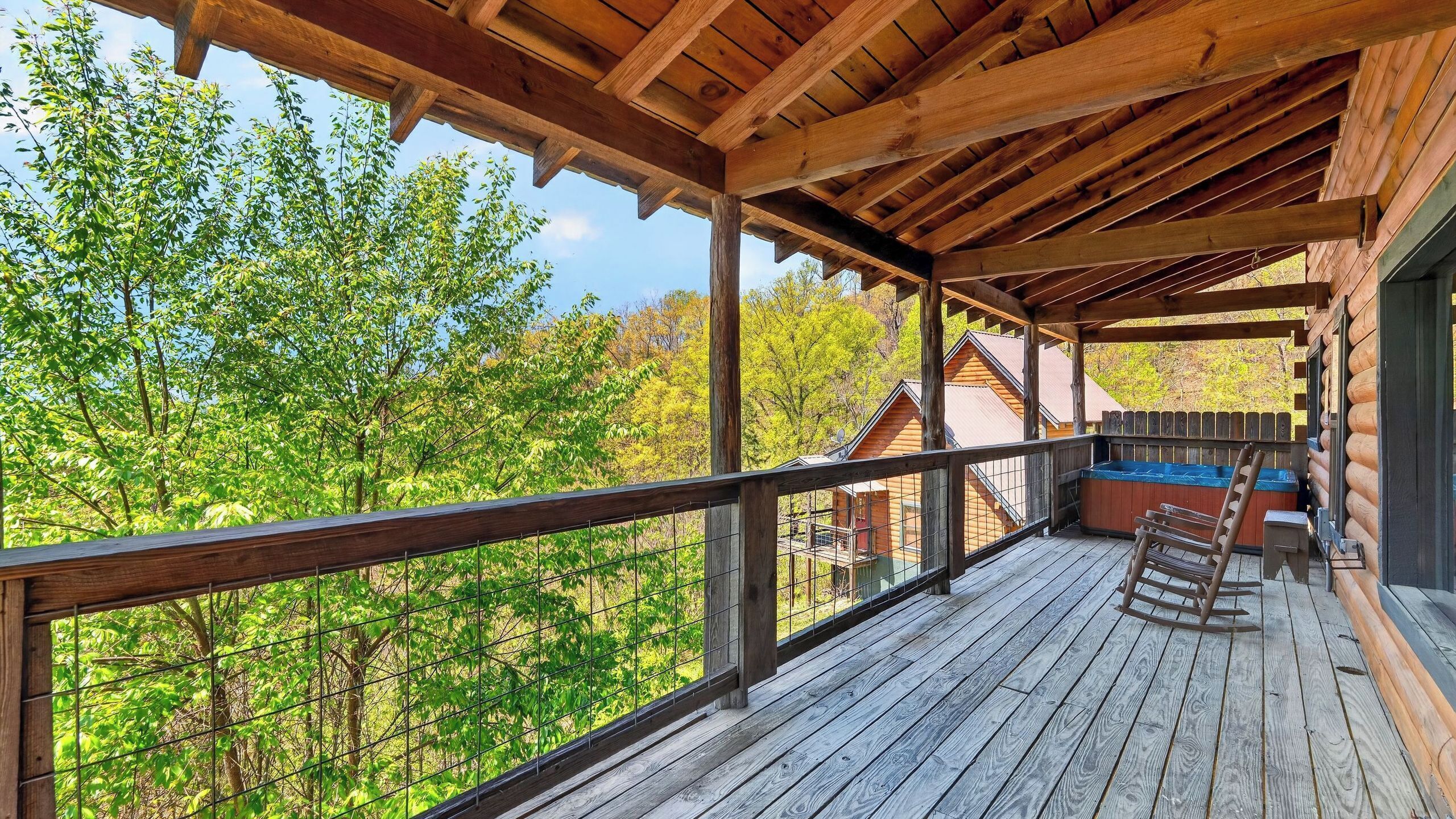 A wooden deck with a railing, a hot tub, and a rocking chair.