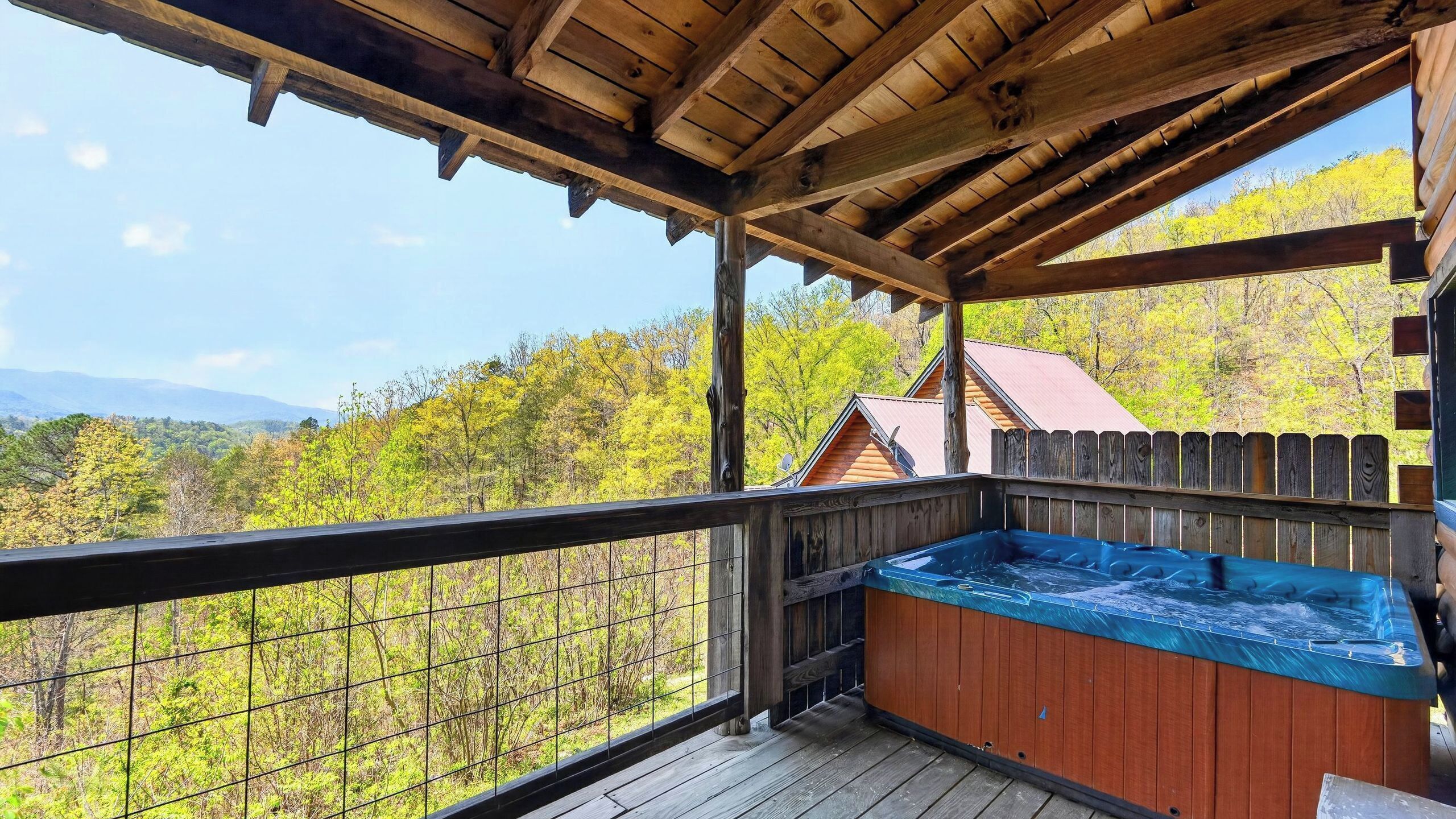 A wooden deck with a hot tub, a wooden fence, and a view of trees and mountains.