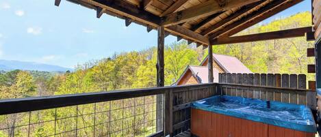A wooden deck with a hot tub, a wooden fence, and a view of trees and mountains.