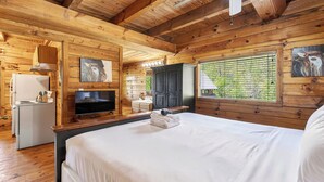 A wooden cabin interior with a bed, TV, kitchenette, and a window with a view. - Sónyah's Cabin by Avantstay Hot Tub + Deck + Firepit + Mountain Views Mins to Downtown (Townsend)