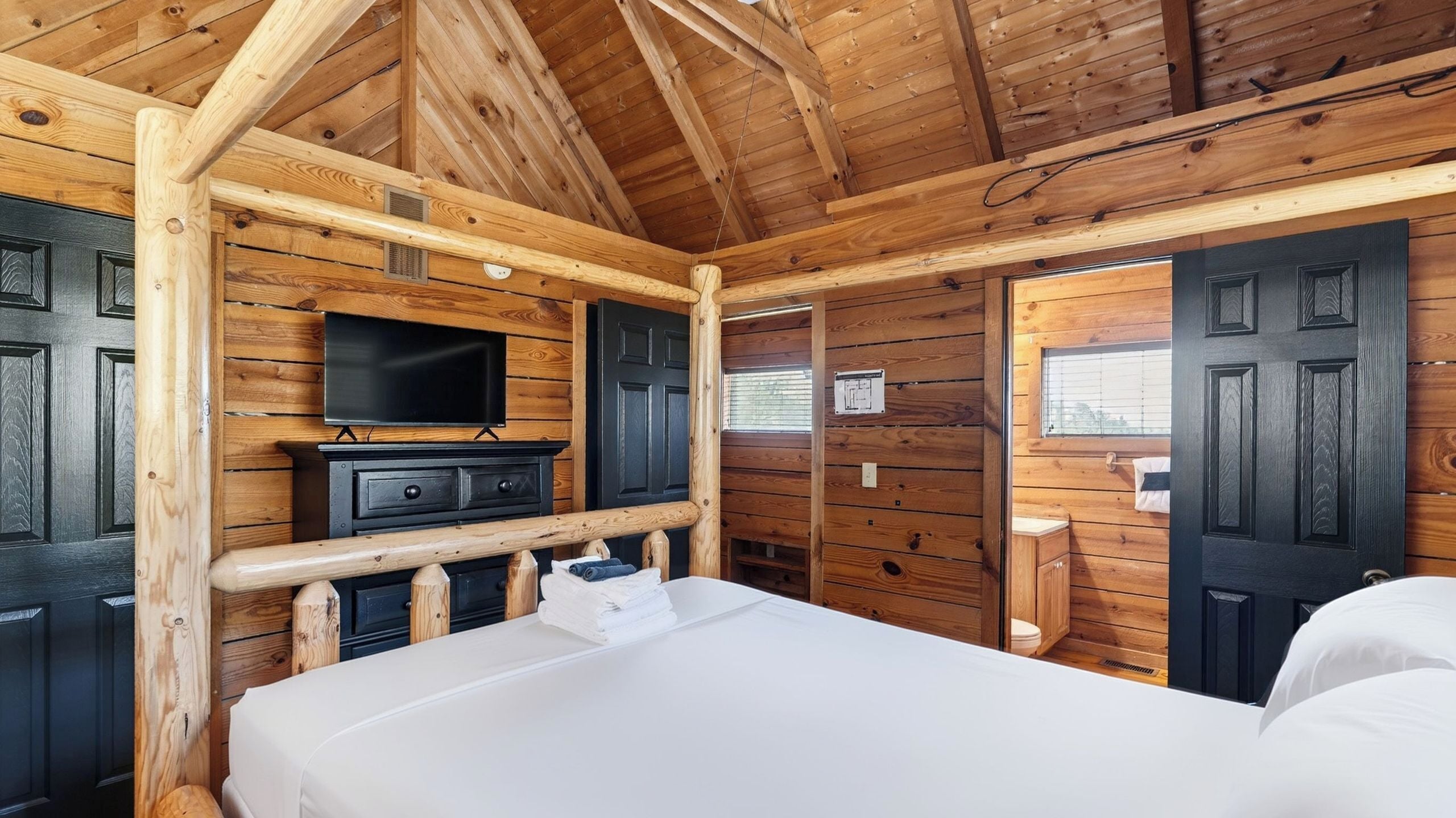 Habitación tipo cabaña de madera con una cama, un televisor y una ventana.