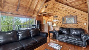 A wooden cabin interior with two leather sofas, a dining area, and a kitchen. - Sónyah's Cabin by Avantstay Hot Tub + Deck + Firepit + Mountain Views Mins to Downtown (Townsend)