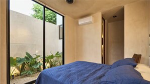 Una camera da letto con un'ampia finestra, un letto con biancheria azzurra e un condizionatore d'aria a parete.