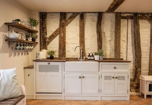 A kitchen with white cabinetry, a wooden countertop, and a stone wall with exposed beams.