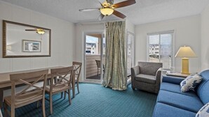 Ein Zimmer mit Deckenventilator, einem Esstisch mit Stühlen, einer Couch, einer Lampe und Blick durch eine Tür.