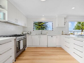 Una cocina moderna con armarios blancos, horno empotrado, un lavamanos y una ventana con vistas a árboles.
