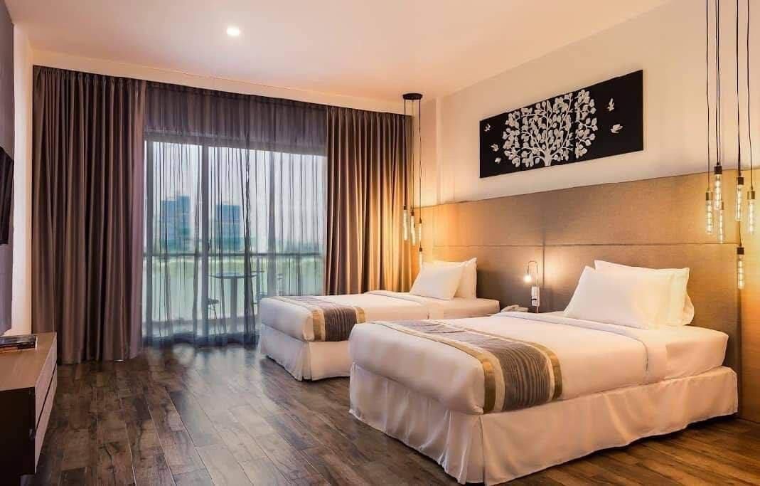A hotel room with two beds, a large window with curtains, a city view, and a wall-mounted artwork.