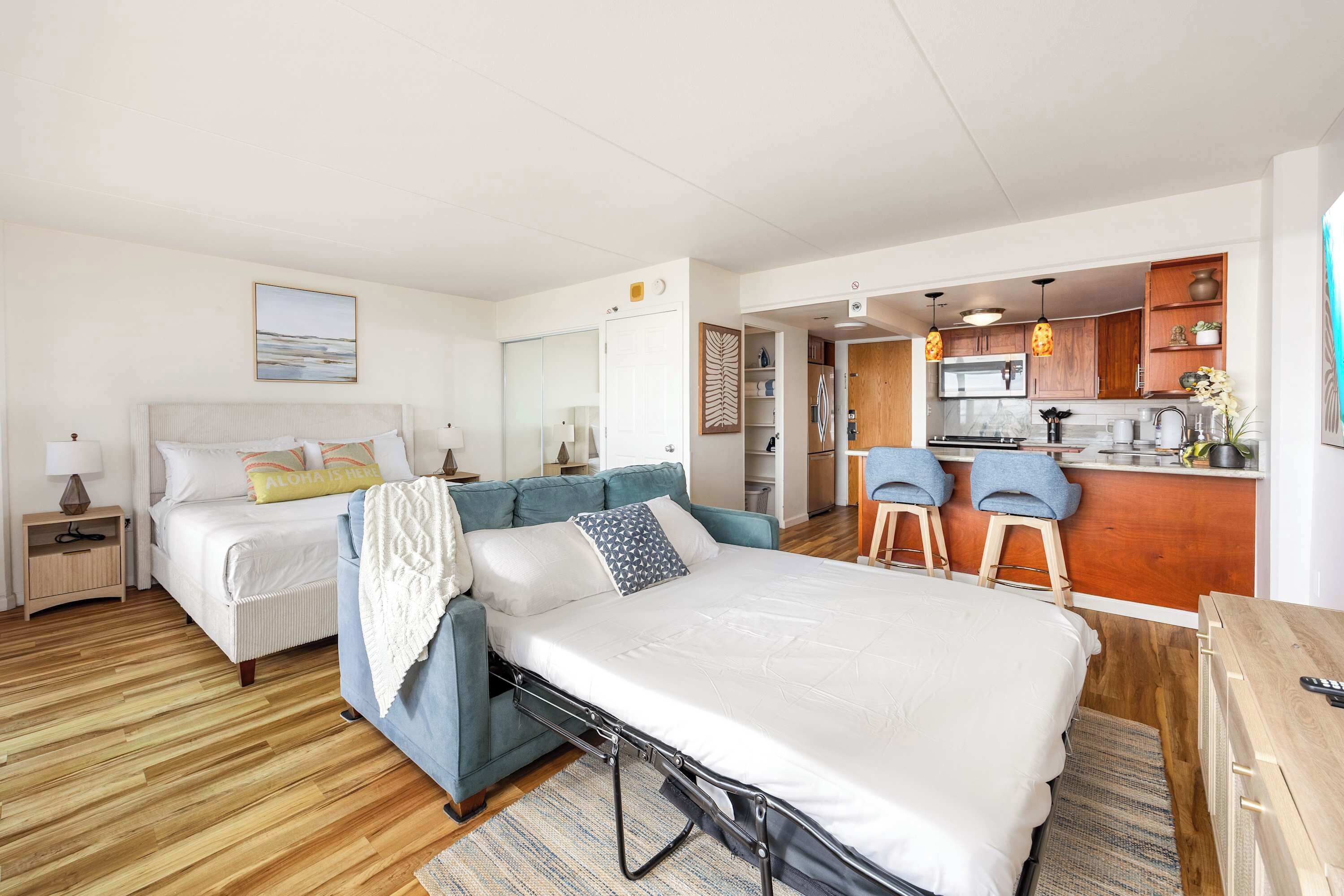 A room with a bed, a sofa, a small kitchen area, and a dining table.
