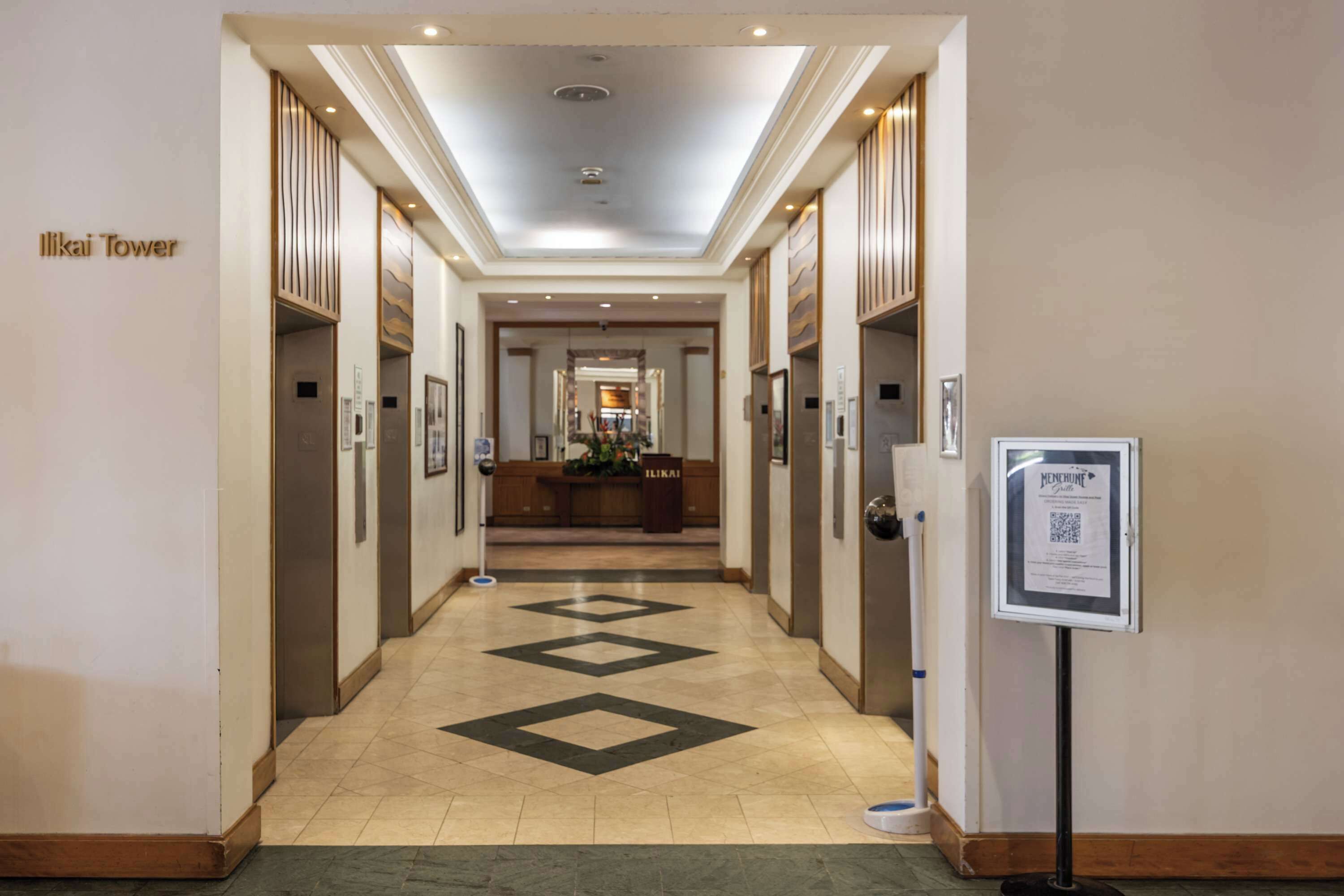 A hotel corridor with a central reception desk, multiple doors, and a floor with a geometric pattern.