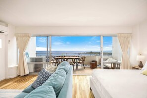 A hotel room with a balcony, a sofa, a bed, a table with chairs, and a view of the sea. - Steps to Beach, 11FL Stunning Ocean Views, 2 Pools (Honolulu)