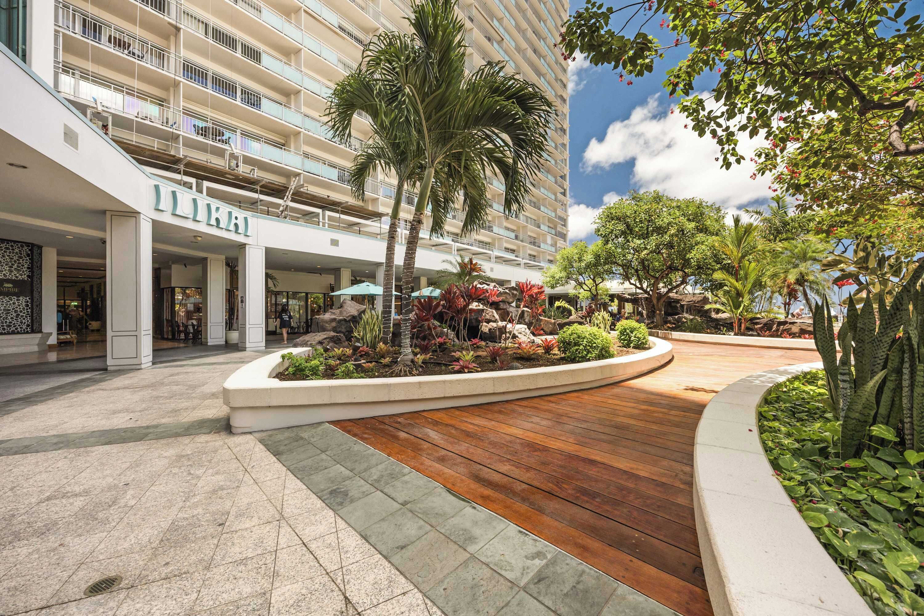 Un hotel de diseño moderno, con un patio central que tiene una terraza de madera, rodeado de abundante vegetación y palmeras.