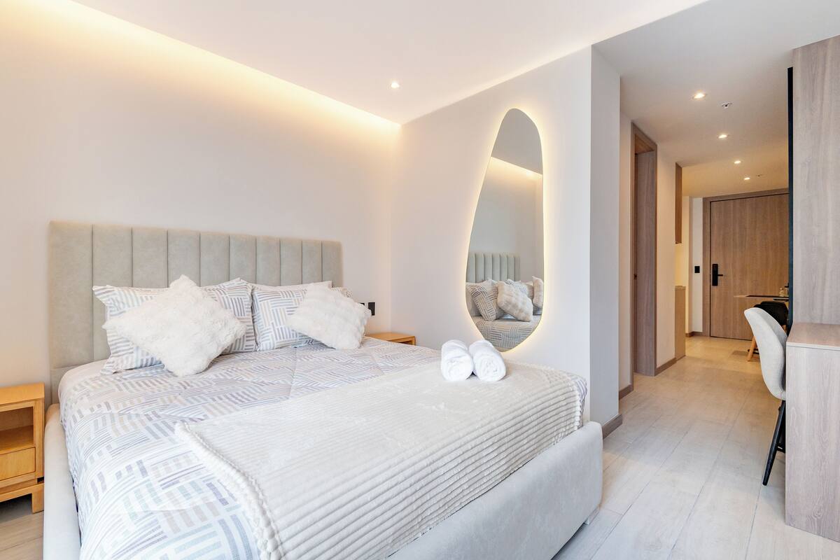 Un dormitorio moderno con una cama grande, un espejo y un espacio de escritorio.