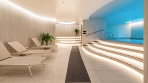 Un espace piscine intérieur moderne, doté de chaises longues, d’un escalier menant à la piscine et d’un comptoir d’accueil.