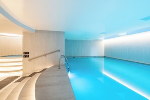 A modern indoor swimming pool with a clear blue water, a metal handrail, and a light-colored wall. - Edificio Adagio by Host Ecuador (Quito)
