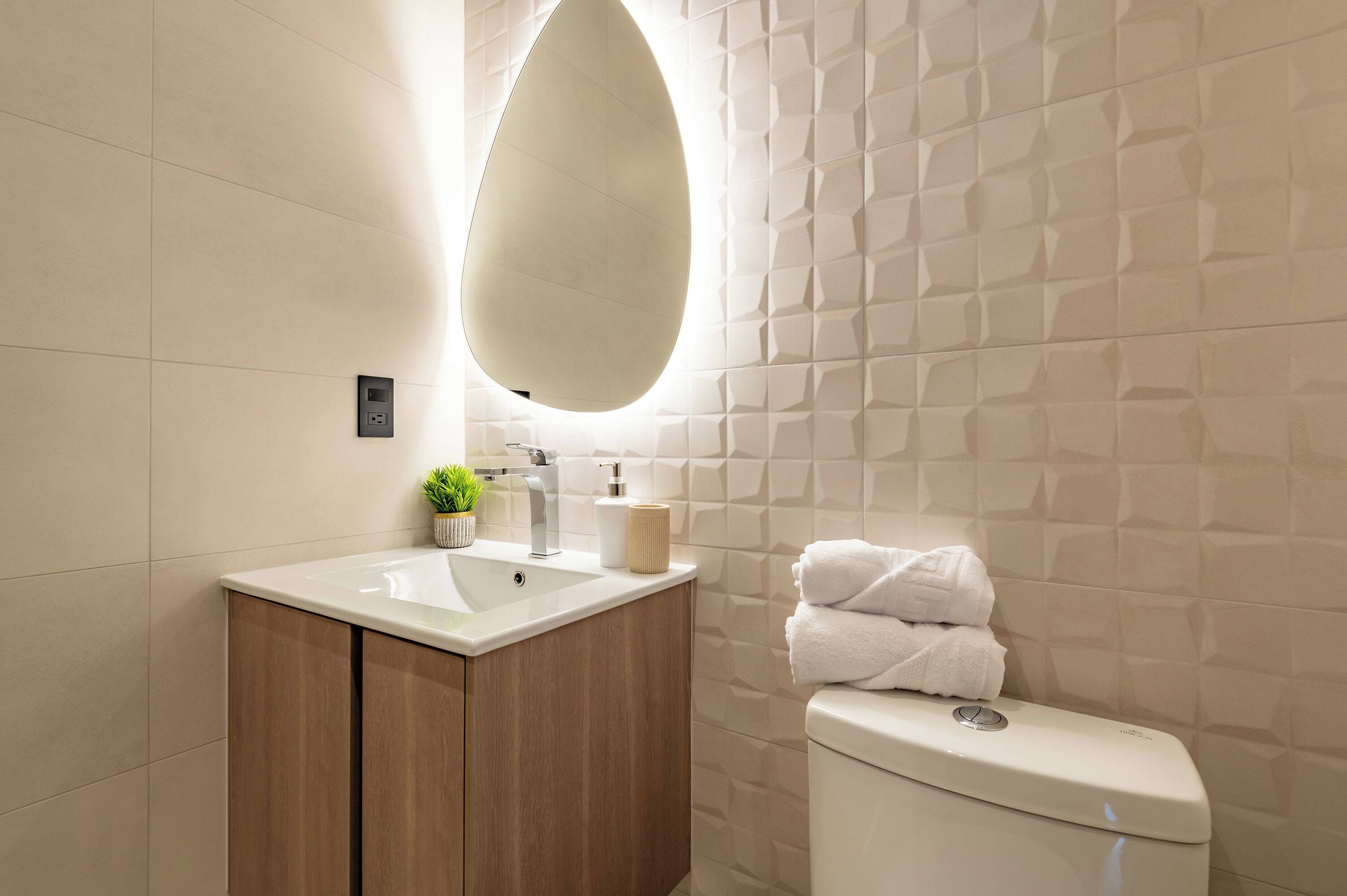 A modern bathroom with a white sink, wooden cabinet, and a toilet with a towel stack.