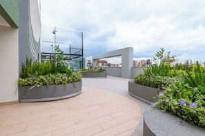 Un giardino pensile con fioriere, un vialetto curvo e vista sulla città.