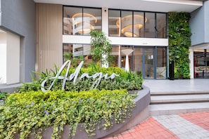 Una entrada moderna a un edificio con un letrero que dice 'Aguas', rodeada de abundante vegetación y una zona de asientos escalonada.