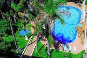 A swimming pool surrounded by palm trees, with lounge chairs and a small rock formation.