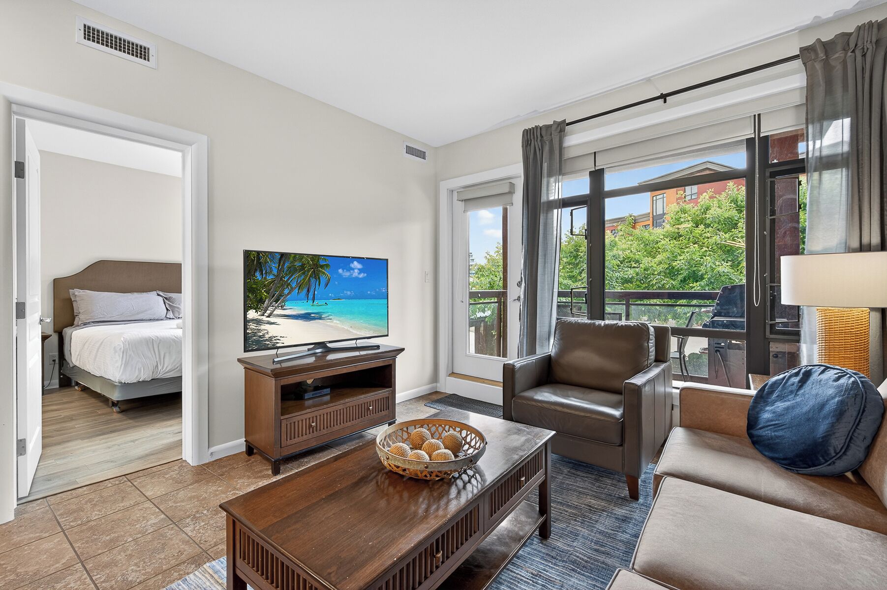 A hotel room with a bed, a TV, a sofa, a coffee table, and a window with a view of the outdoors.