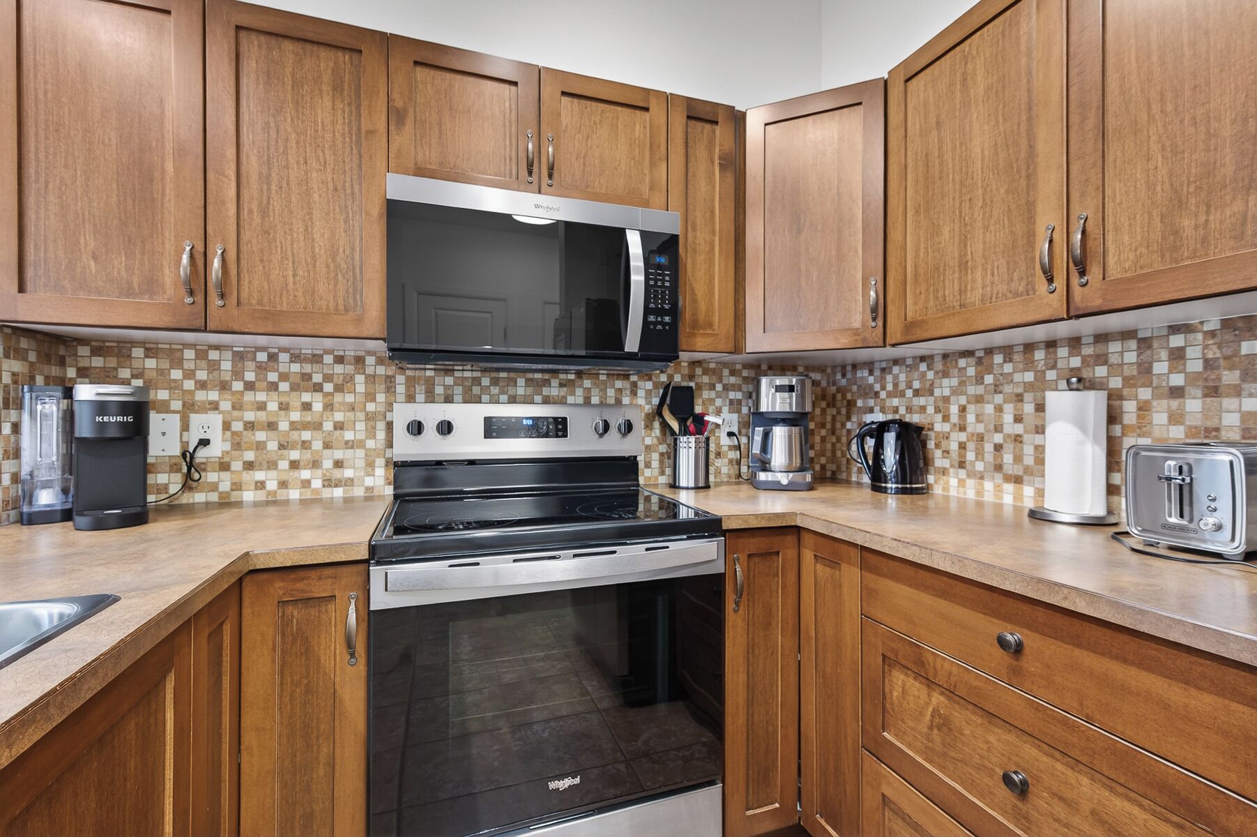 Una cocina con armarios de madera, microondas, estufa, cafetera y tostadora.