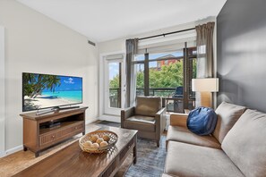 Un salon moderne avec un téléviseur, un canapé en cuir et une vue sur la plage, grâce à de grandes fenêtres.