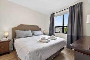 Ein Hotelzimmer mit Bett, Nachttischen, Schreibtisch und einem fensterbepflanzten Fenster.